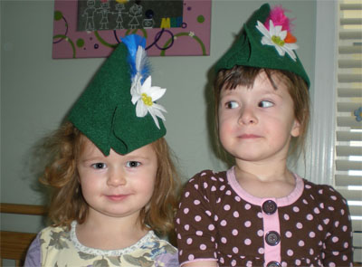 Two girls wearing green felt Edelweiss hats with feathers and flowers